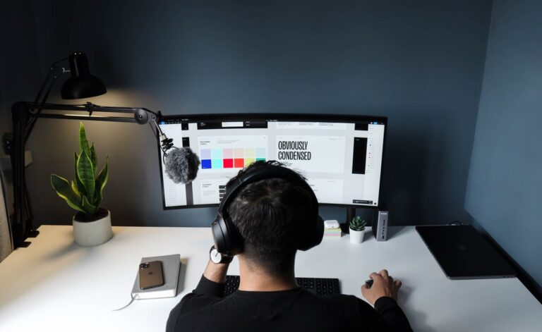 Rapaz usando computador de mesa, com mouse e teclado sem fio. Na tela ele está selecionando paleta de cores e estilo de fonte (condensado), simbolizando marca mista