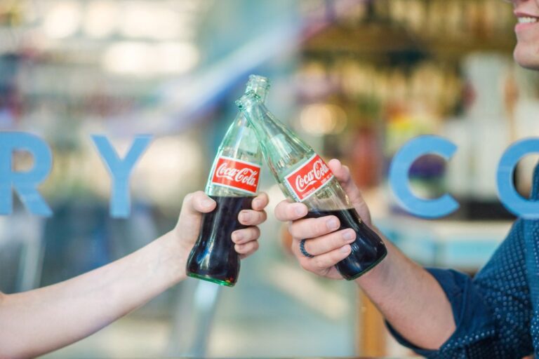 Duas pessoas segurando uma garrafa de vidro de Coca-Cola cada uma, simbolizando marca tridimensional