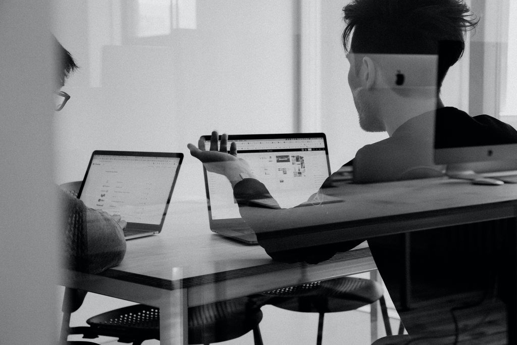 Duas pessoas em uma mesa de reunião, usando notebook, simbolizando a dúvida de se é possível registrar uma marca gratuitamente